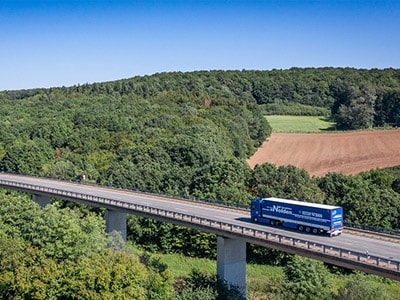 LKW von Nolden Logistics GmbH fährt auf einer Brücke umgeben von Wald